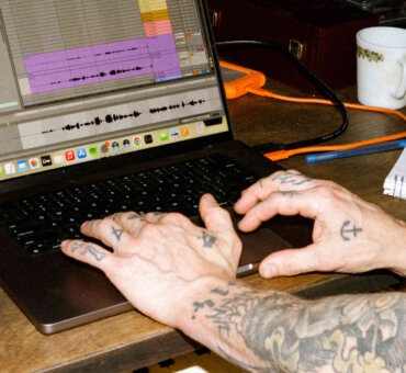 Person with tattooed arms typing on a laptop keyboard